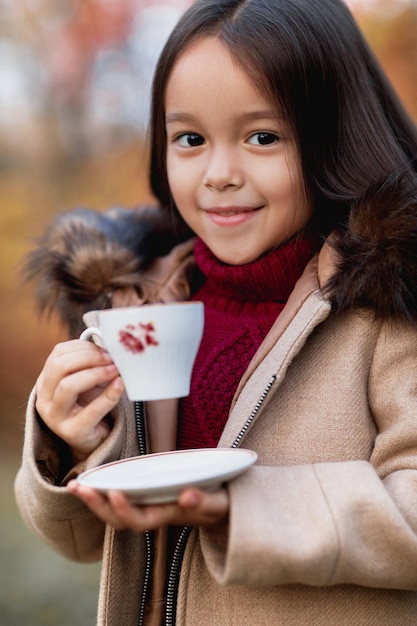 秋の公園で暖かいお茶を飲む少女