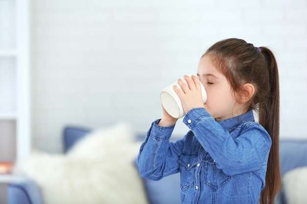 リビング ルームでカップから水を飲む少女