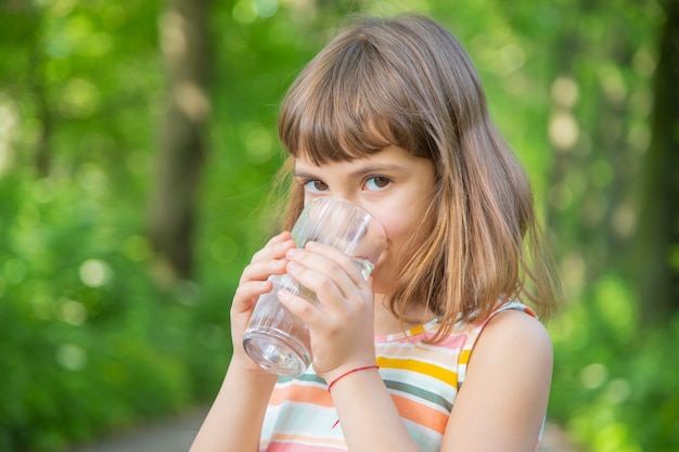 Маленькая девочка пьет воду из стекла