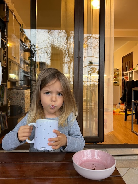 Little girl drinks milk from a huge cup on the balcony