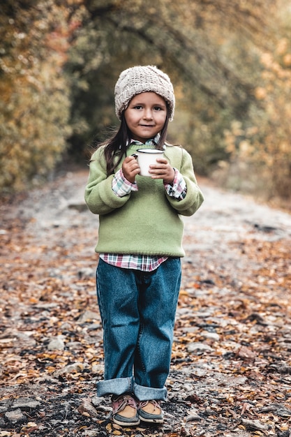 小さな女の子が秋の公園でお茶を飲む