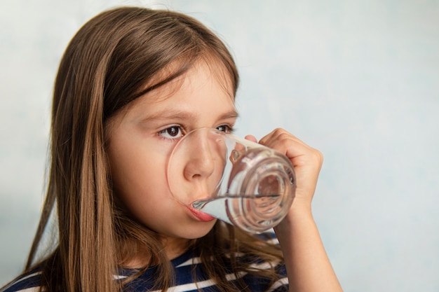 Una bambina beve l'acqua da una tazza di vetro. bambina che tiene un bicchiere d'acqua. sete d'acqua