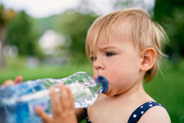 Little girl drinks water from a plastic bottle closeup