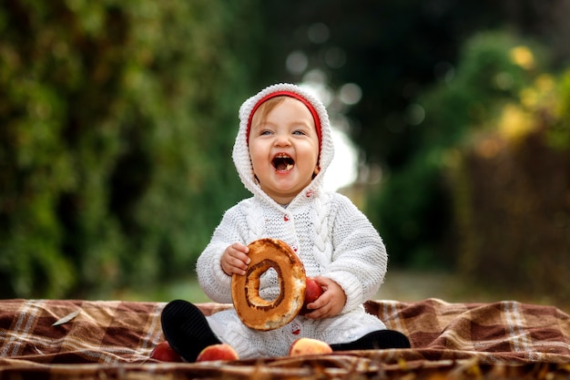 毛布の上に座って公園でベーグルを食べる少女