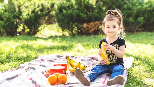 Bambina che mangia banana al picnic nel parco