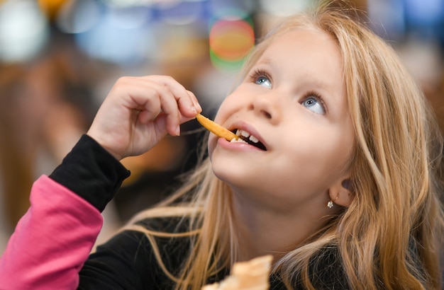 ファーストフードカフェでフライドポテトを食べる少女。