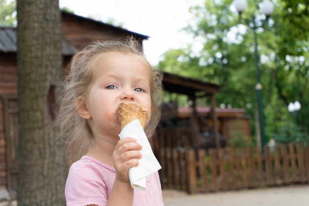 Little girl eating an ice-cream in the park in summer hot day