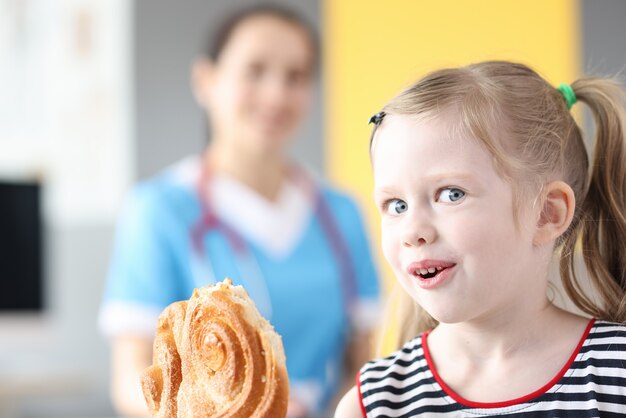 Bambina che mangia una confezione dolce sullo sfondo del dottore