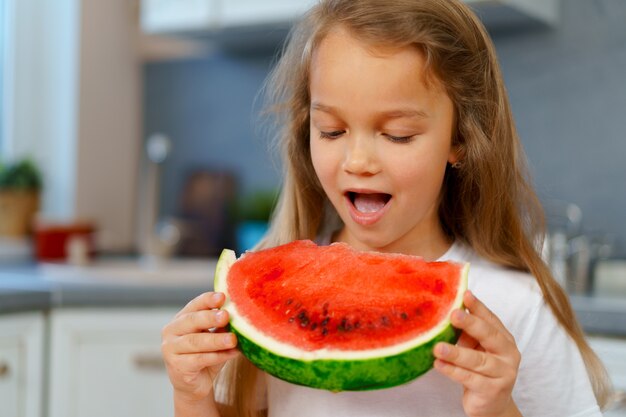 Little girl eating watermelon piece in the kitchen