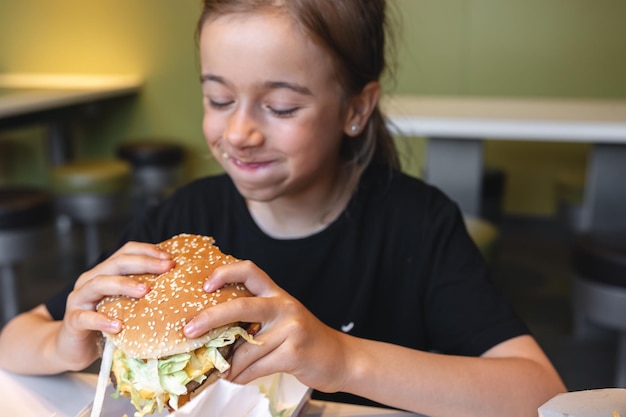 小さな女の子が食欲をそそるハンバーガーのクローズ アップを食べる