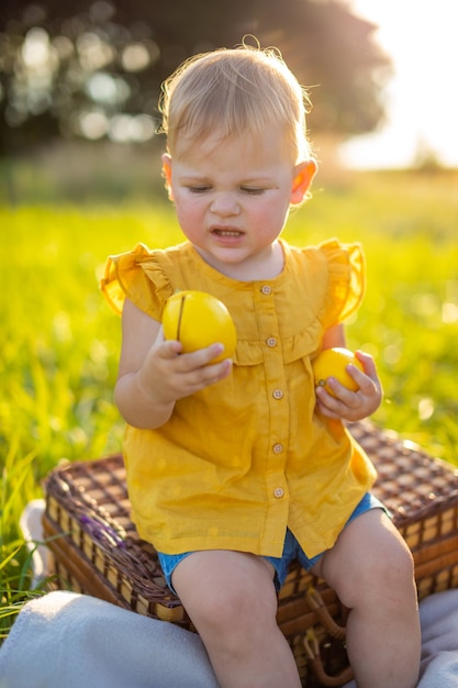 Little girl eats fresh fruits on a picnic at sunset lights in nature