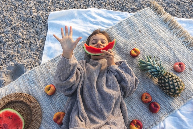 Little girl eats fruit lying on a blanket on the beach