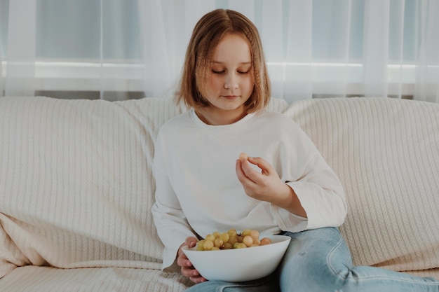 小さな女の子がソファでブドウを食べる健康的な食事