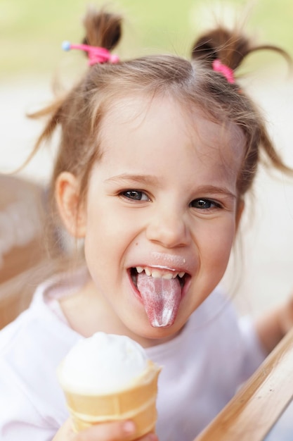 Foto la bambina mangia il gelato e mostra la lingua.