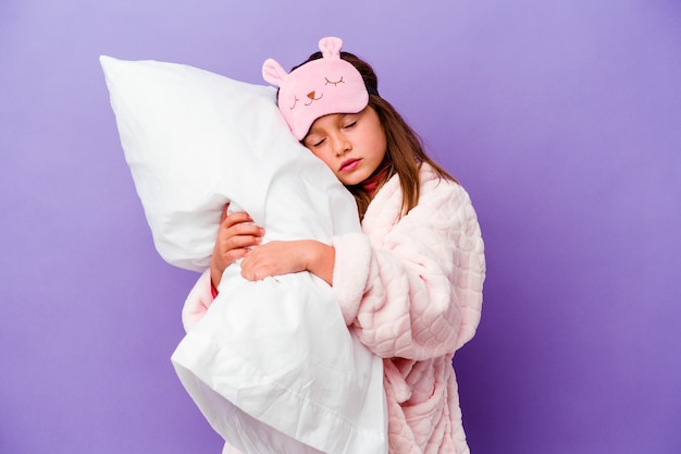 Little girl embracing a pillow happy isolated on purple