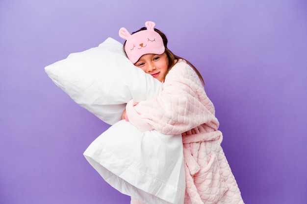 Little girl embracing a pillow happy isolated on purple