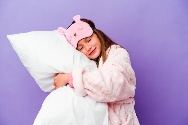 Little girl embracing a pillow happy isolated on purple