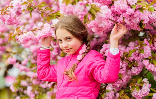 Little girl enjoy spring Kid on pink flowers of sakura tree background Kid enjoying pink cherry blossom Tender bloom Pink is the most girlish color Bright and vibrant Pink is my favorite