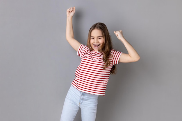 Little girl expressing winning gesture with raised fists and screaming celebrating victory