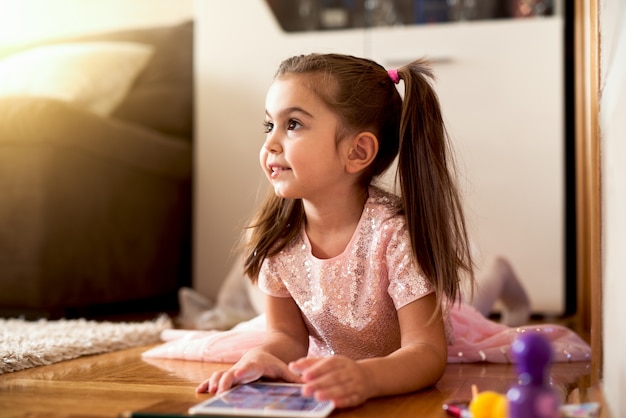 Little girl in fancy dress lying floor playing on tab