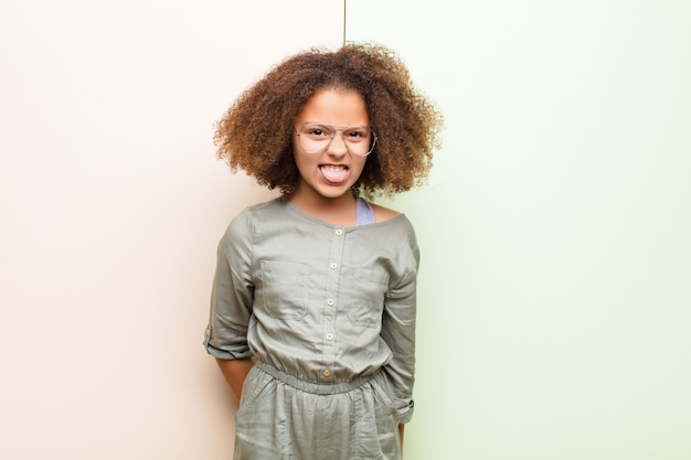 Photo little girl feeling disgusted and irritated, sticking tongue out, disliking something nasty and yucky against wall