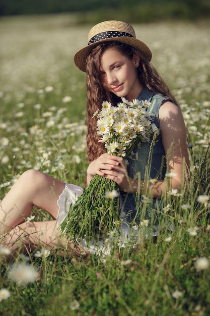 Little girl in a field of daisy flowers. Teen girl in hat and dress enjoys spring in daisy field