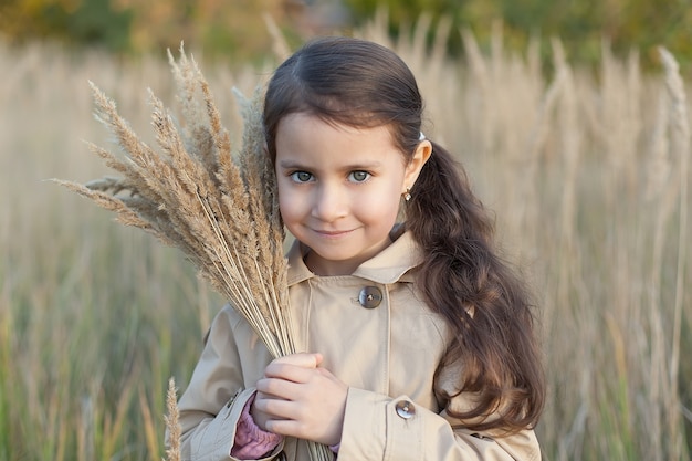 little girl in the field holds a bouquet of wheat.