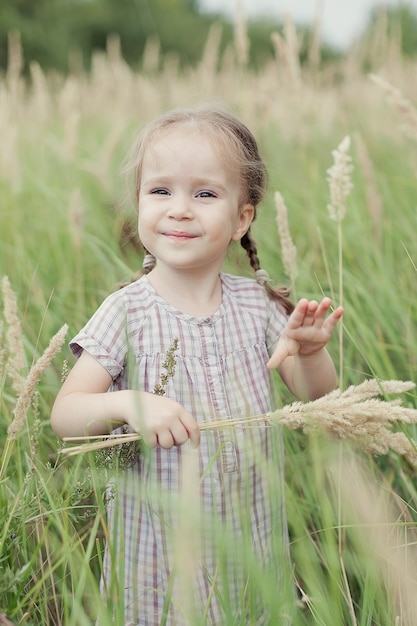 여름날에 작은 이삭이 있는 들판에 있는 어린 소녀. 행복한 어린 시절의 개념.
