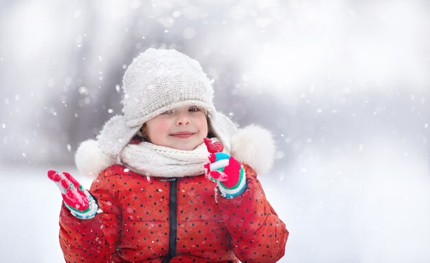 ふわふわの帽子をかぶった少女が雪の降る冬の日に歩く