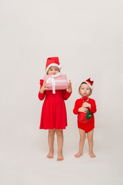 어린 소녀와 공간의 복사본과 함께 흰 벽에 크리스마스 선물과 함께 빨간 모자에 전체 길이 소년