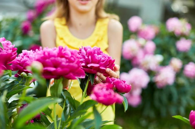 Little girl in the garden in bushes of peonies child touch the flower