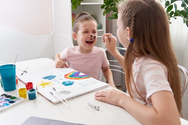 Photo little girl getting her face painted by older sister at the table