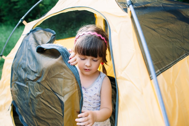 Little girl getting out from tent in forest