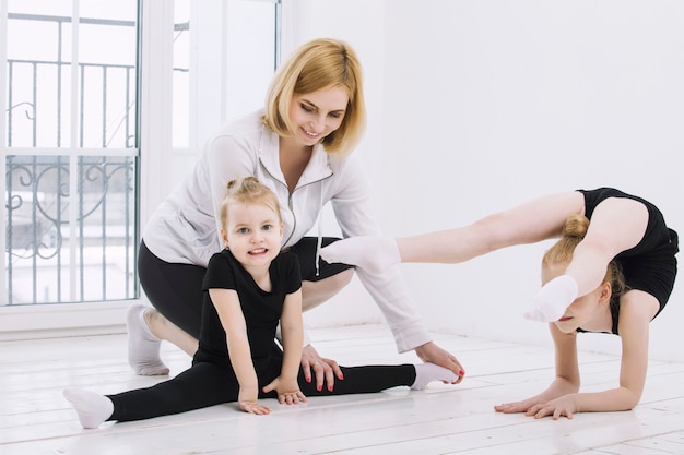 Ginnaste e ballerina di bambine che fanno stretching con un allenatore in una stanza luminosa felice e carina