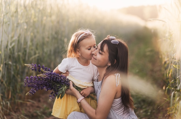 A little girl gives a bouquet of lupines to her mother on the field in the summer. Concept of love and happy family