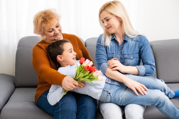 A little girl gives a bouquet of tulips to her mom and grandmother. They celebrate Mother's Day. They have a traditional family holiday.