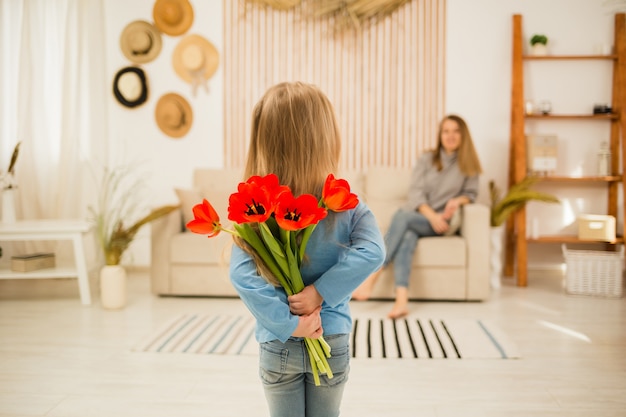 Little girl gives red tulips to her mother in the room