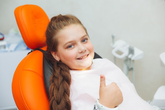 A little girl gives a thumbs up and smiles while sitting in a dentist's chair medicine and healthcare