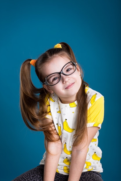 Little girl in glasses and banana T-Shirt on blue background