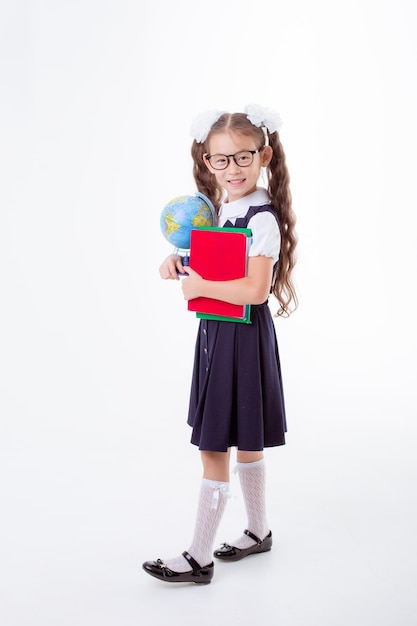 little girl in glasses and a school uniform holds a book and a globe isolated on a white background