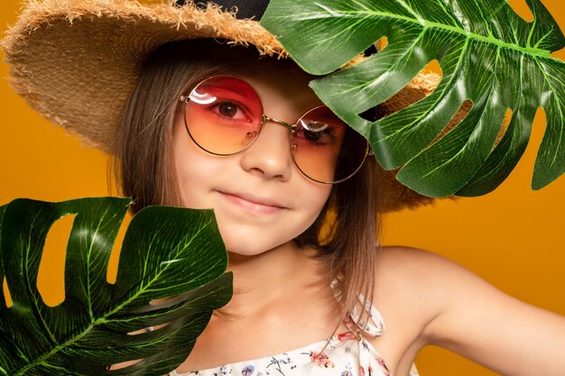 Little girl in glasses and a straw hat on a yellow background in the studio