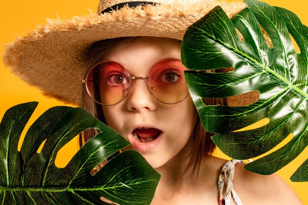 Little girl in glasses and a straw hat on a yellow background in the studio