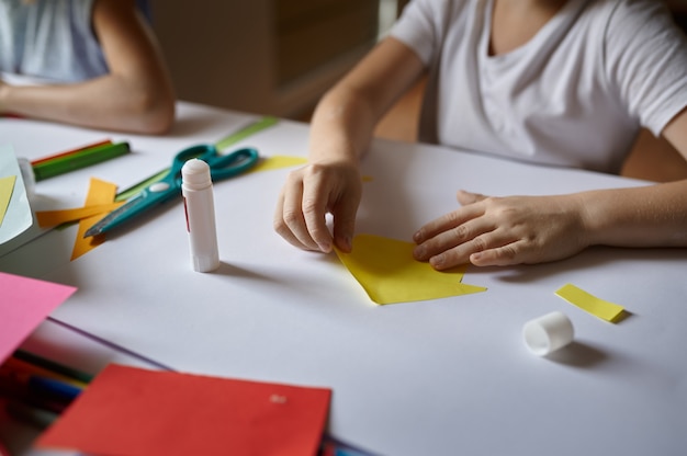 Little girl glues colored paper, kid in workshop