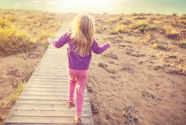 Little girl goes by boardwalk in sea shore at sunrise