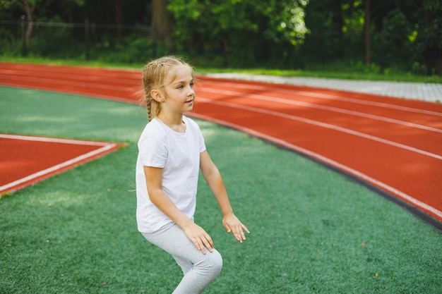 小さな女の子が芝生の上でスポーツに参加します子供はスタジアムでトレーニングする前にウォーミングアップを行います子供のスポーツと健康的なライフスタイル