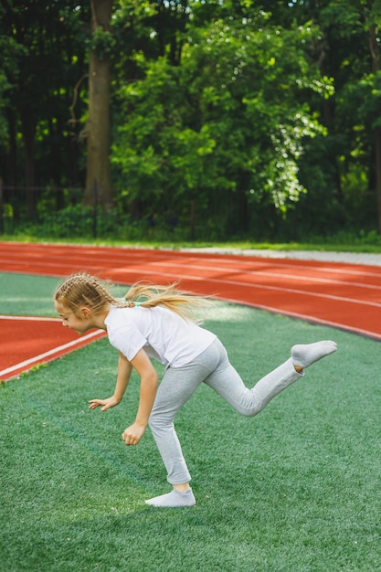 어린 소녀가 잔디밭에서 운동을 하기 위해 입장합니다. 어린이는 경기장에서 훈련하기 전에 워밍업을 합니다. 어린이 스포츠와 건강한 생활 방식