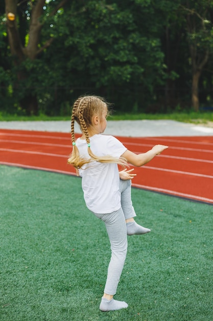 A little girl goes in for sports on the grass the child does a warmup before training at the stadium Children's sports and healthy lifestyle