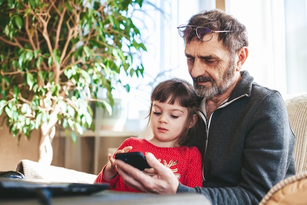 Little girl and grandfather using smartphone