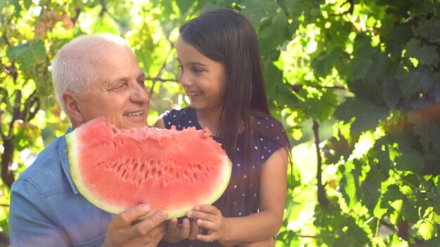 little girl and grandfather with watermelon smile and eat