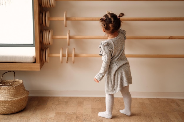 Photo little girl in a gray dress plays with wooden abacus in the children's room learns to count wooden rings educational wooden toys for children